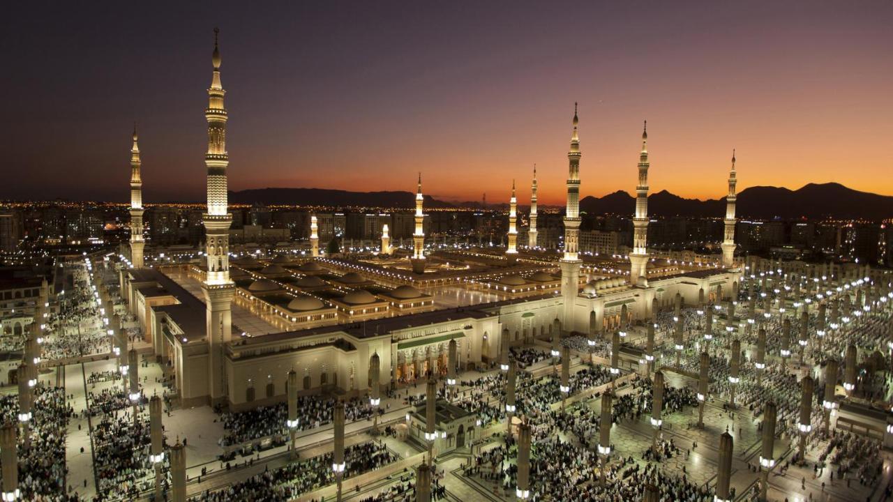 Intercontinental Dar Al Iman Madinah By Ihg Hotel Медина Екстериор снимка The photo depicts an aerial view of a large mosque complex during sunset. The mosque features multiple tall minarets, which are intricately designed and illuminated, giving the scene a stunning appearance as the sky transitions from daylight to dusk.