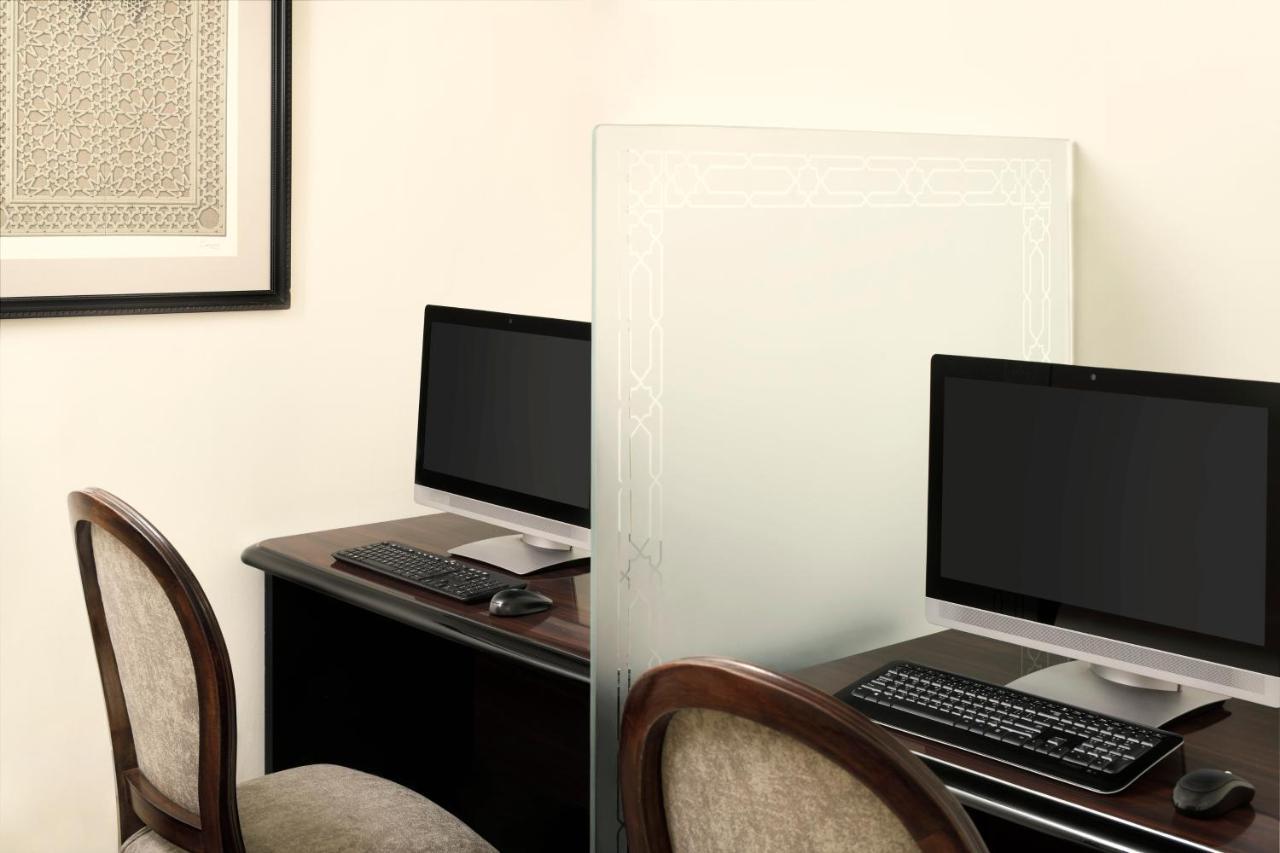 Intercontinental Dar Al Iman Madinah By Ihg Hotel Медина Екстериор снимка The photo shows a workspace featuring two computers set up on a dark wooden desk. Each computer has a monitor and a keyboard. A frosted glass partition is placed between the two workstations, providing some privacy. In the background, there is a fram
