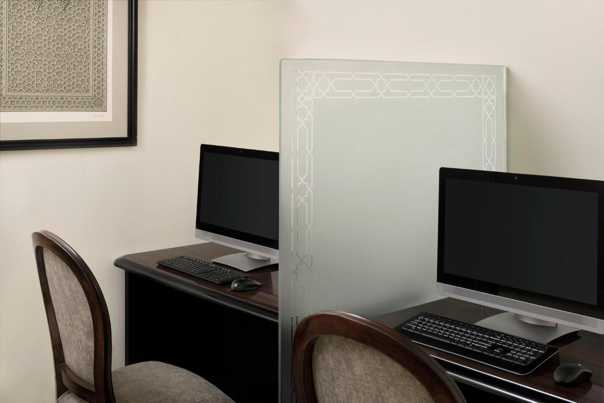 Intercontinental Dar Al Iman Madinah By Ihg Hotel Медина Екстериор снимка The photo shows a small office or workspace area featuring two computer stations. Each station has a black monitor, a keyboard, and appears to be set up on a dark wooden desk. A translucent glass partition is placed between the two workstations, prov