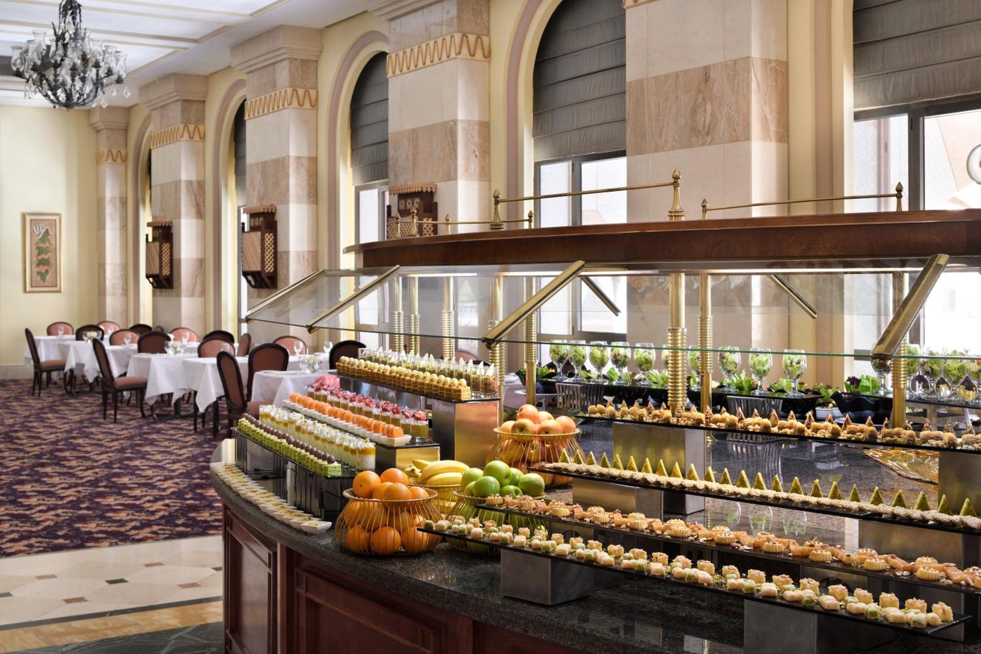 Intercontinental Dar Al Iman Madinah By Ihg Hotel Медина Екстериор снимка The photo depicts an elegant dining area featuring a buffet-style display. In the foreground, a beautifully arranged buffet counter showcases an array of desserts, including miniature pastries and colorful fruit. The setting has a sophisticated ambia