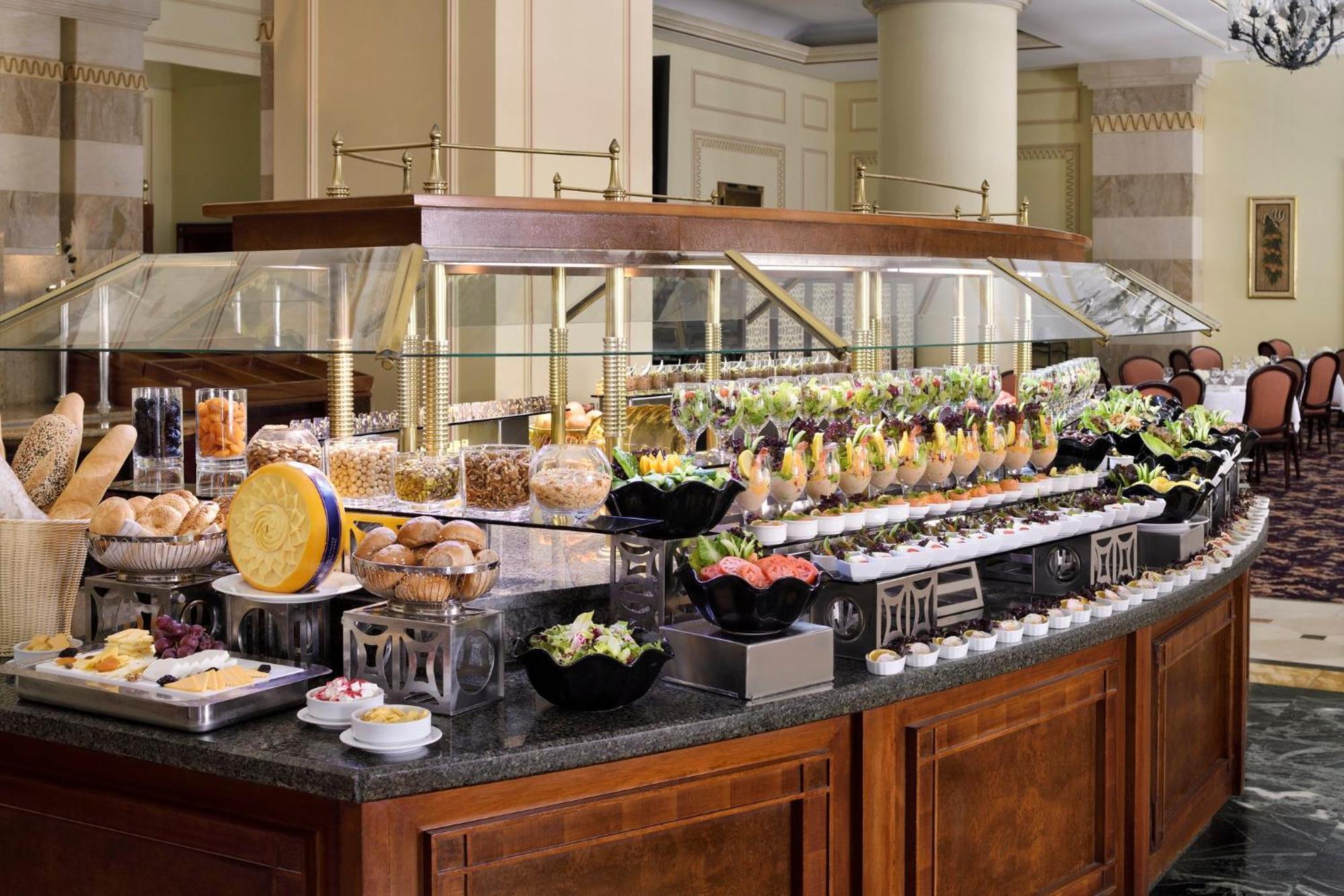 Intercontinental Dar Al Iman Madinah By Ihg Hotel Медина Екстериор снимка The photo shows an elegantly arranged buffet with a variety of food items. There is a large, curved wooden display with glass covers, showcasing an assortment of dishes. These include different types of breads and rolls, salads, garnishes, and desser