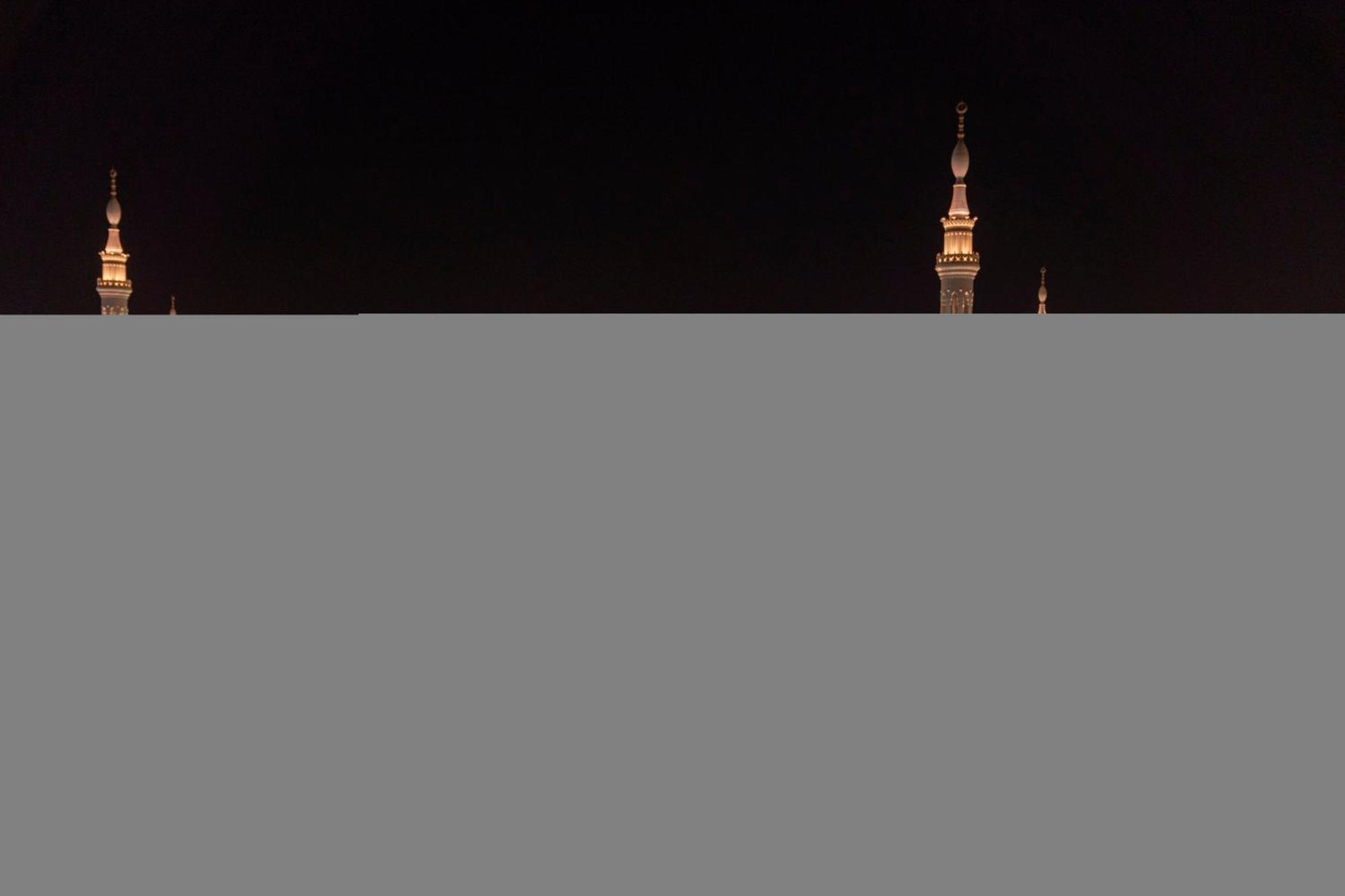 Intercontinental Dar Al Iman Madinah By Ihg Hotel Медина Екстериор снимка The image appears to show a night scene featuring tall structures with pointed tops, likely minarets, illuminated against a dark background. The lighting creates a striking contrast, highlighting the architectural details of the structures. The overa