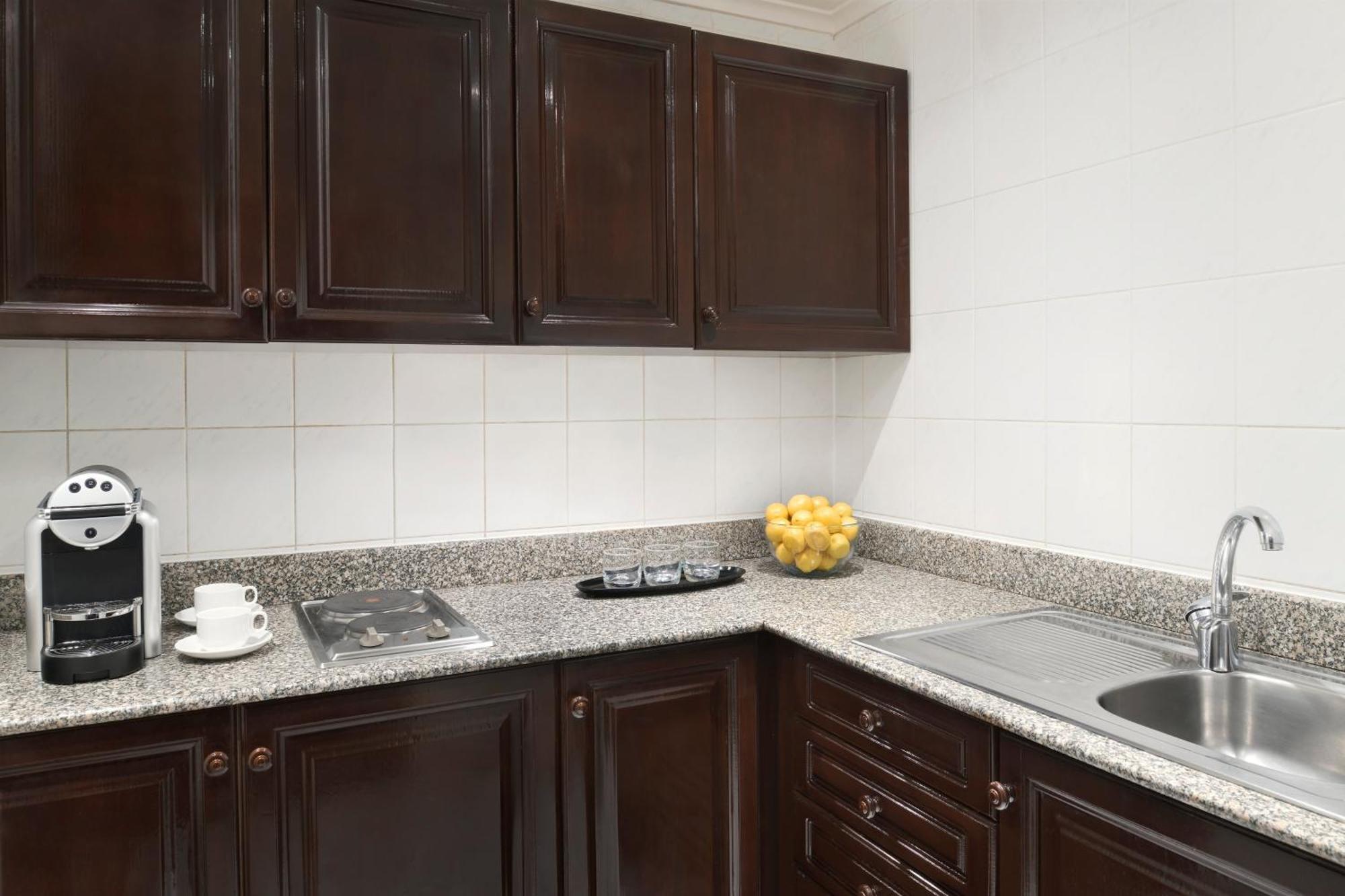 Intercontinental Dar Al Iman Madinah By Ihg Hotel Медина Екстериор снимка The photo shows a kitchen with dark wooden cabinetry and a light-colored countertop. There are a few appliances visible, including a coffee machine and a stovetop with burners. To the right, there is a sink, and a bowl of yellow lemons is placed on t