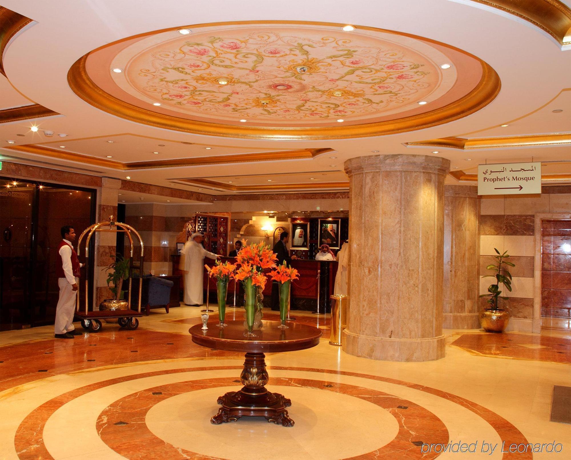 Intercontinental Dar Al Iman Madinah By Ihg Hotel Медина Интериор снимка The photo depicts a luxurious hotel lobby. The ceiling features an ornate design with floral patterns, adding elegance to the space. In the center of the lobby, there is a decorative table with a bowl or vase of bright orange flowers. The flooring is