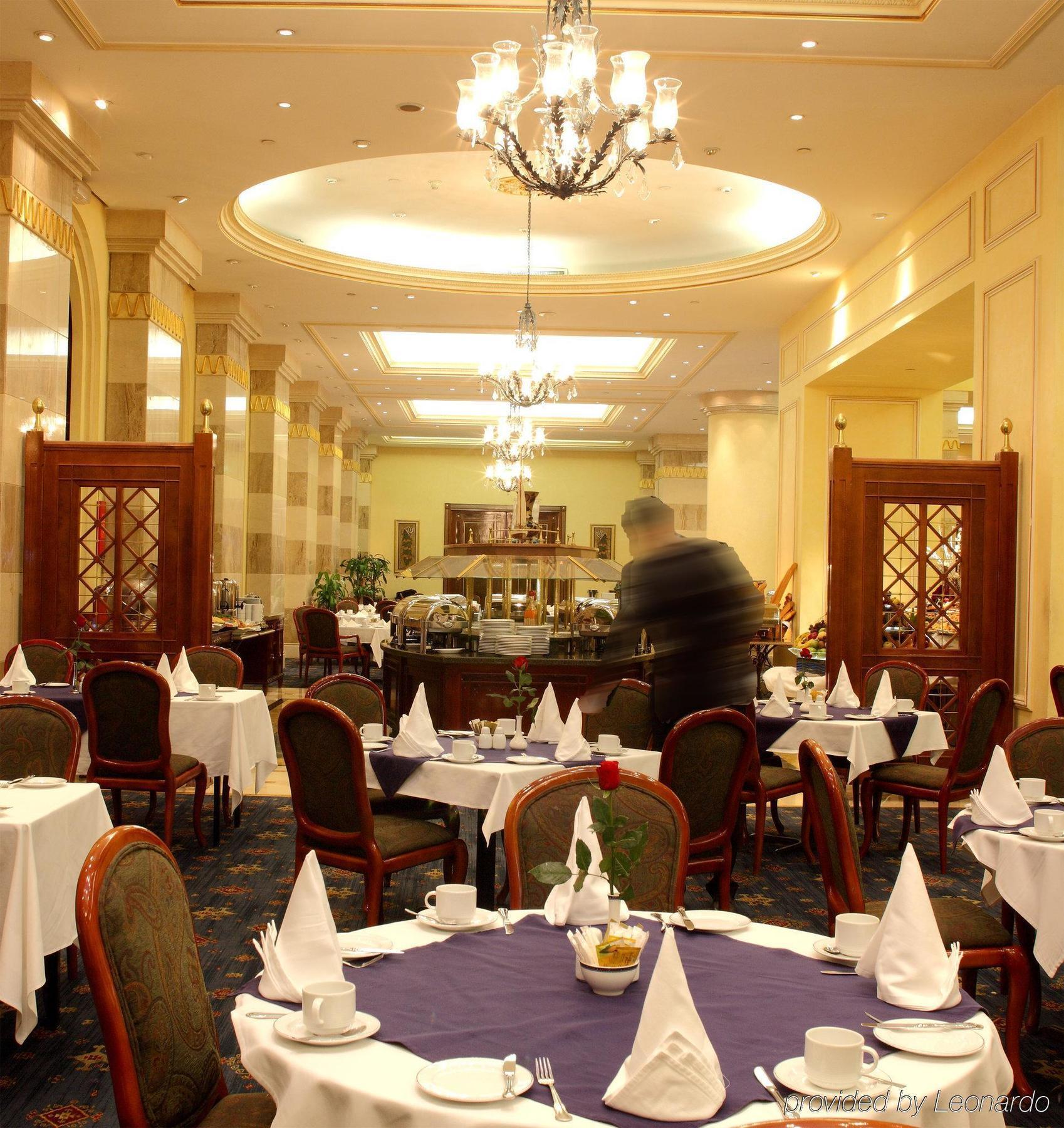 Intercontinental Dar Al Iman Madinah By Ihg Hotel Медина Ресторант снимка The photo depicts an elegant restaurant interior. It features round tables covered with white tablecloths, each set with plates, cutlery, and folded napkins arranged into triangles. The space has a warm, inviting atmosphere with a mix of decorative e
