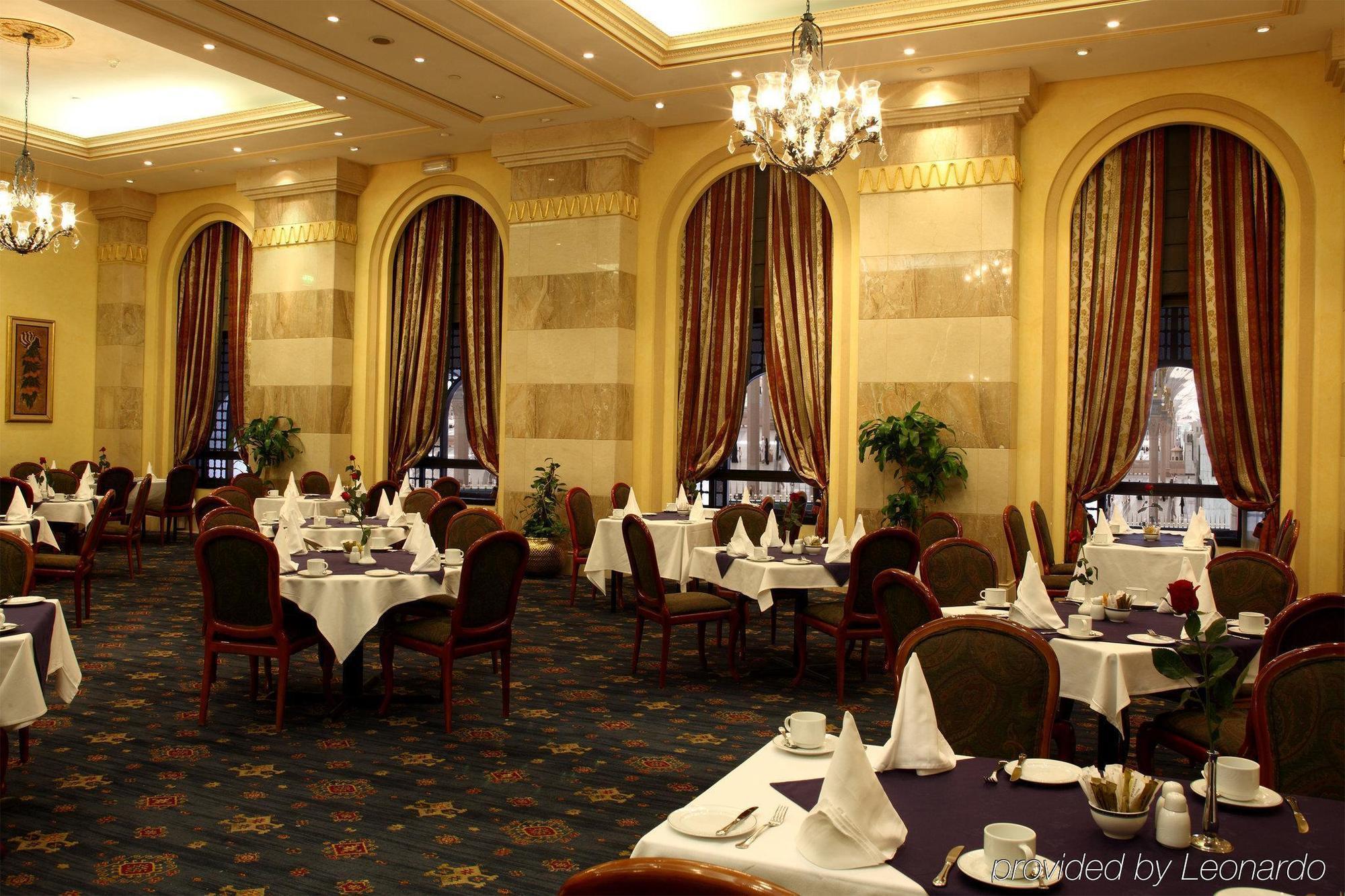 Intercontinental Dar Al Iman Madinah By Ihg Hotel Медина Ресторант снимка The photo depicts an elegant restaurant interior. The space features ornate decor with tall windows draped in rich, patterned curtains. Tables are neatly set with white tablecloths and napkins, and there are plush chairs arranged around them. The flo