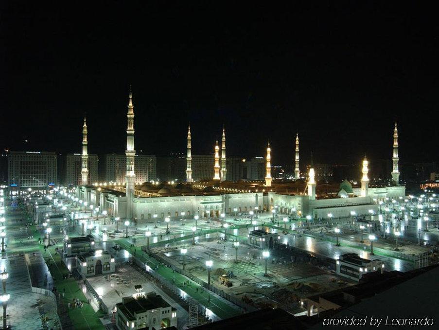 Intercontinental Dar Al Iman Madinah By Ihg Hotel Медина Удобства снимка The image shows the illuminated landscape of a mosque complex at night. It features several tall minarets, which are typically part of Islamic architecture, adorned with lights. The mosque's central building is also brightly lit, surrounded by an ope